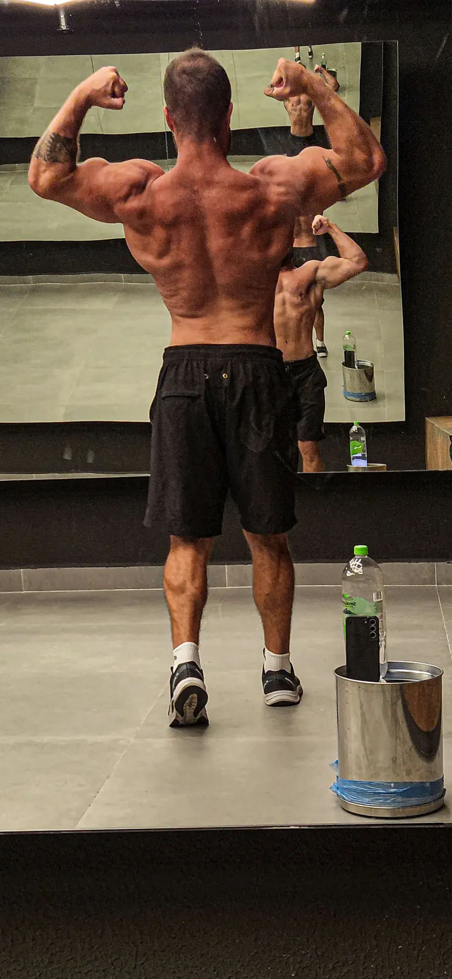 Montinho Personal de costas em pose de duplo bíceps, mostrando a definição de costas e ombros — personal trainer que atende os condomínios de Alphaville