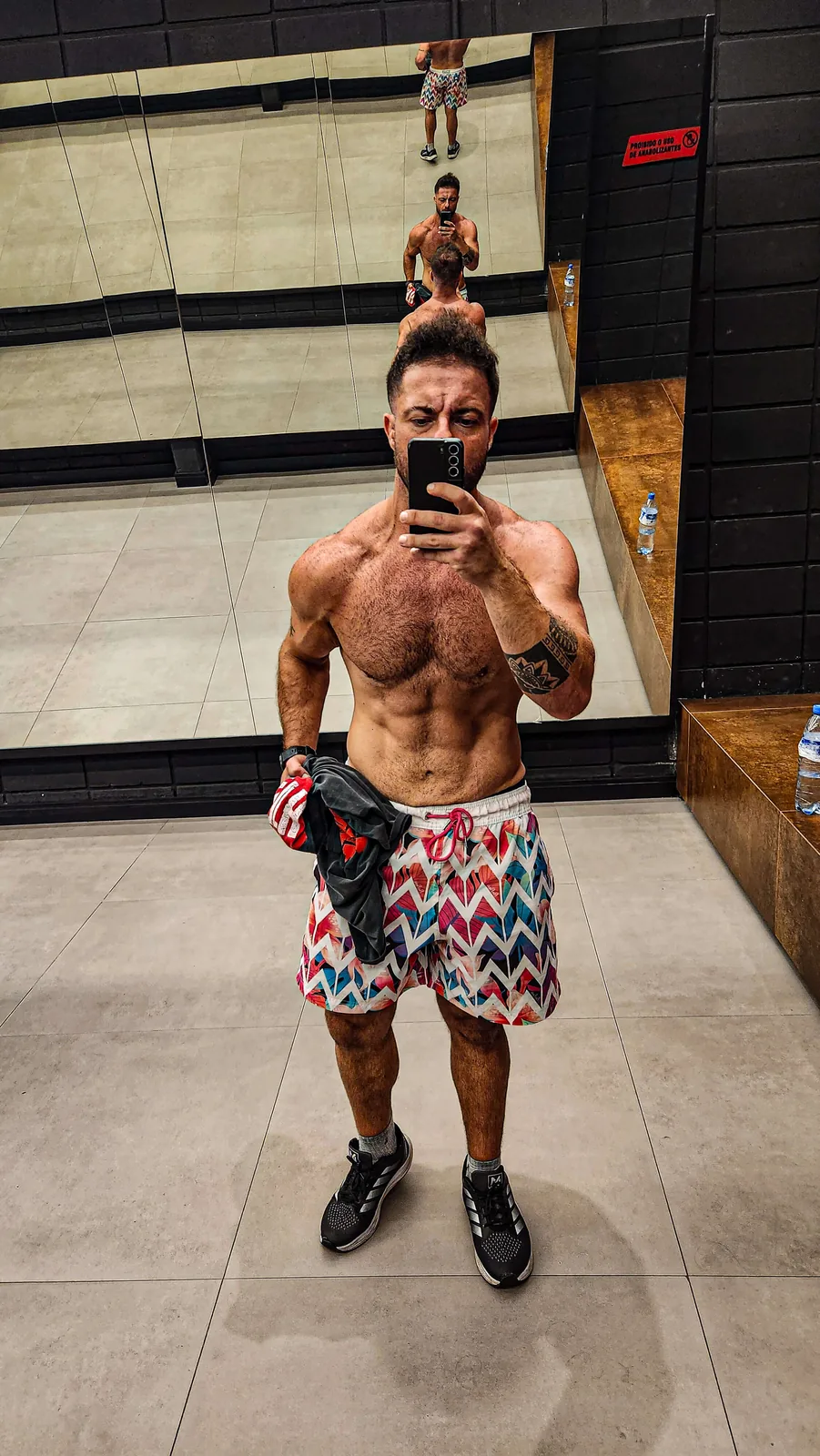 Montinho Personal sem camisa, de bermuda estampada, em selfie de corpo inteiro no espelho da academia — personal trainer destacado pelo portal para quem treina em Taboão da Serra